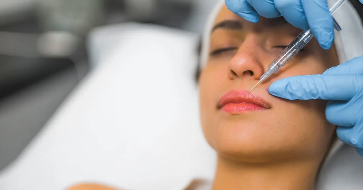Aesthetic injector administering a hyaluronic acid dermal filler injection to a woman's lower lip area for subtle, natural enhancement.