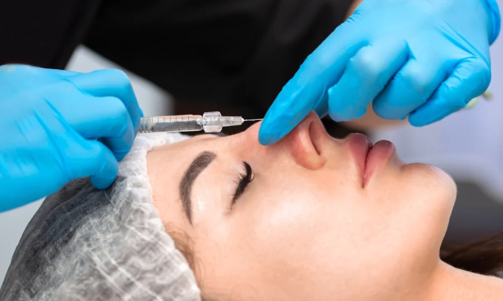 Close-up of a patient receiving a nose injection during a Non-Surgical Nose Job in Delray Beach, FL, with a gloved practitioner holding a syringe at the nasal bridge.